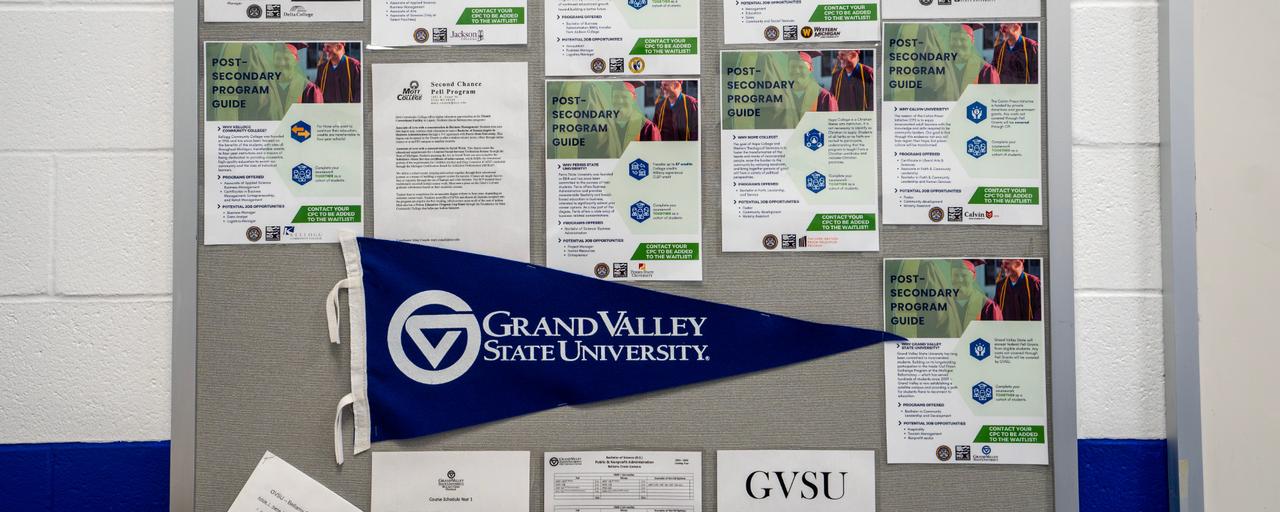 Corkboard displaying posters for several higher education programs in Michigan prisons